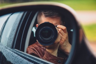 Imagen de persona realizando vigilancia con cámara de fotos desde interior de vehículo.